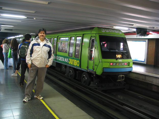 Ein Zug auf einem Bahngleis mit Menschen zu links und einem Dach oben im Bild.