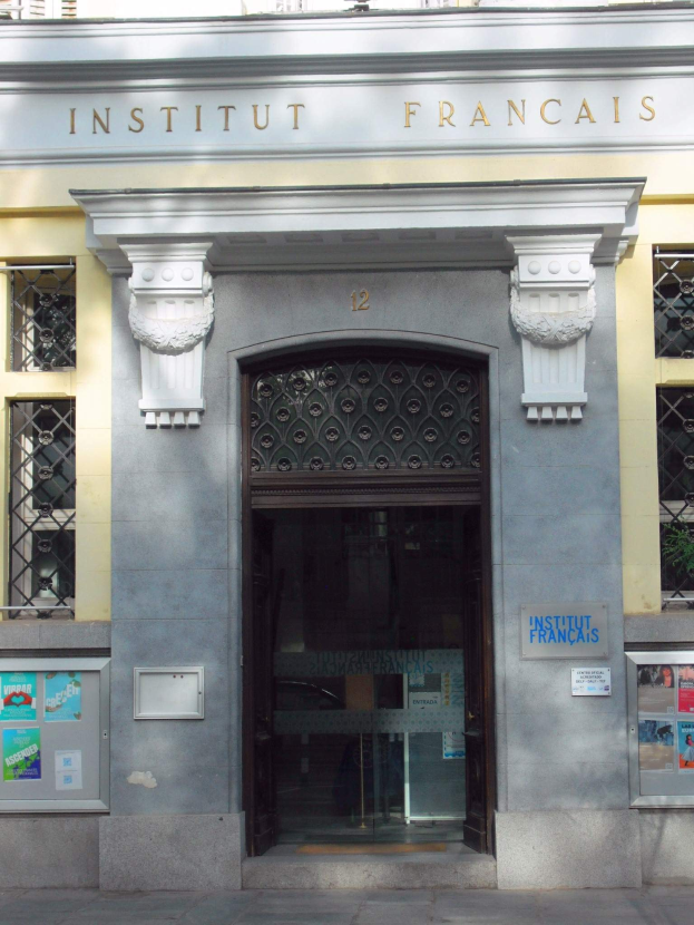 Der Eingang des Institut Français in Paris, ein Gebäude mit Fenstern, einer Tür und Plakaten an der Wand, mit einer Straße unten.