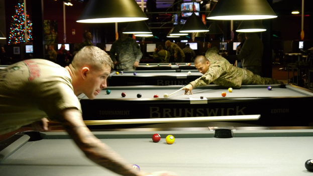 Ein Raum mit Snookertischen, Spielern auf beiden Seiten, hängenden Lampen, einem Weihnachtsbaum in einer Ecke und Bildschirmen mit Punkteständen.