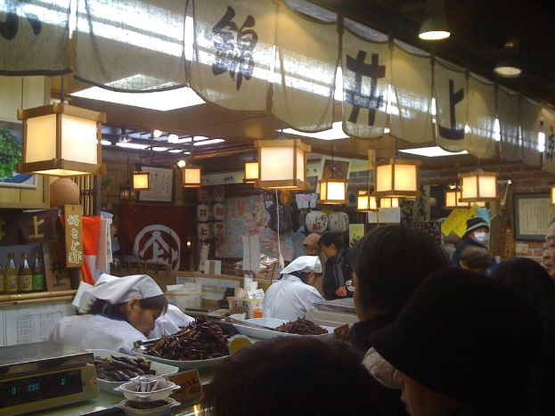 Mitarbeiter arbeiten hinter einer Theke in einem Restaurant mit Gegenständen und Kunden davor und verschiedenen Gegenständen wie Soßenflaschen, Menüs, Kleidung und Lampen im Hintergrund.