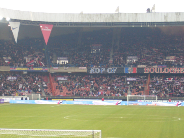 Ein Rasenstadionboden mit Torpfosten auf beiden Seiten, Zuschauern im Hintergrund und zahlreichen Werbetafeln in der Mitte und darüber.