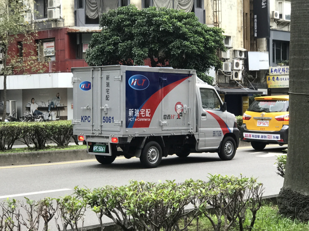 Ambulanz auf einer Straße neben einem Baum mit Fahrzeugen, Gebäuden und anderen Objekten im Hintergrund.