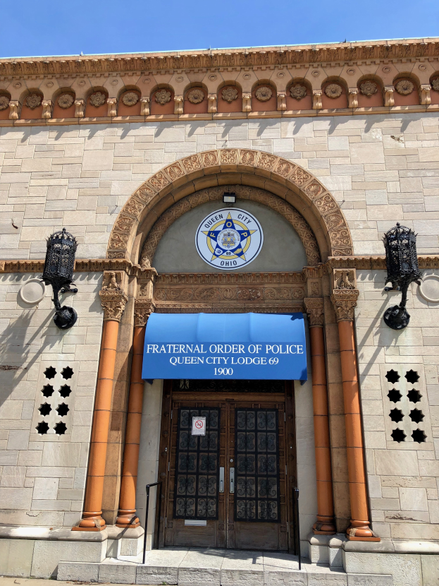 Das Gebäude der Fraternal Order of Police in Queen City, mit einem blauen Vordach, beleuchteten Säulen und einer Tafel mit Text an der Wand, unter einem sichtbaren Himmel.