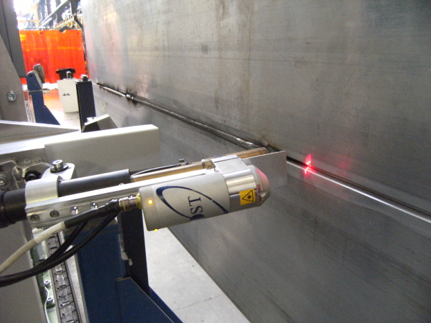 Eine Laserschneidmaschine in einer Fabrik, die helles Licht abstrahlt, mit einer Wand auf der rechten Seite und ein paar Gegenständen im Hintergrund.