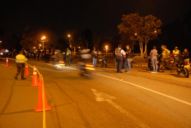 Männer und Fahrräder sind auf einer Straße mit orangenen Fahrstreifen auf der linken Seite, mit Bäumen und Lichtern im Hintergrund.