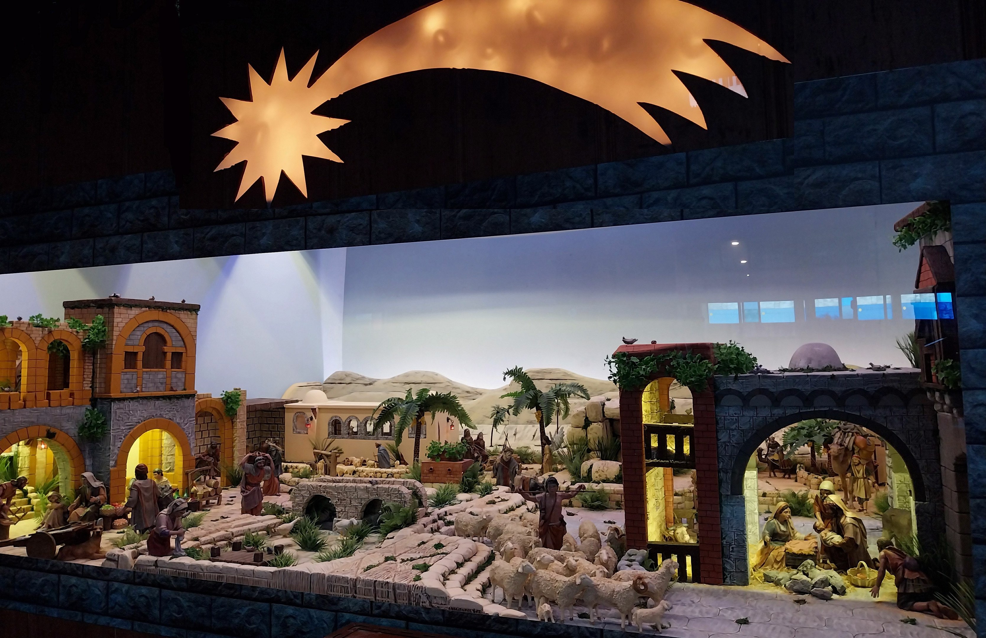 Eine Krippe in einem Museum, mit Menschen, Tieren, Häusern, Bäumen und anderen Gegenständen, beleuchtet von oben.