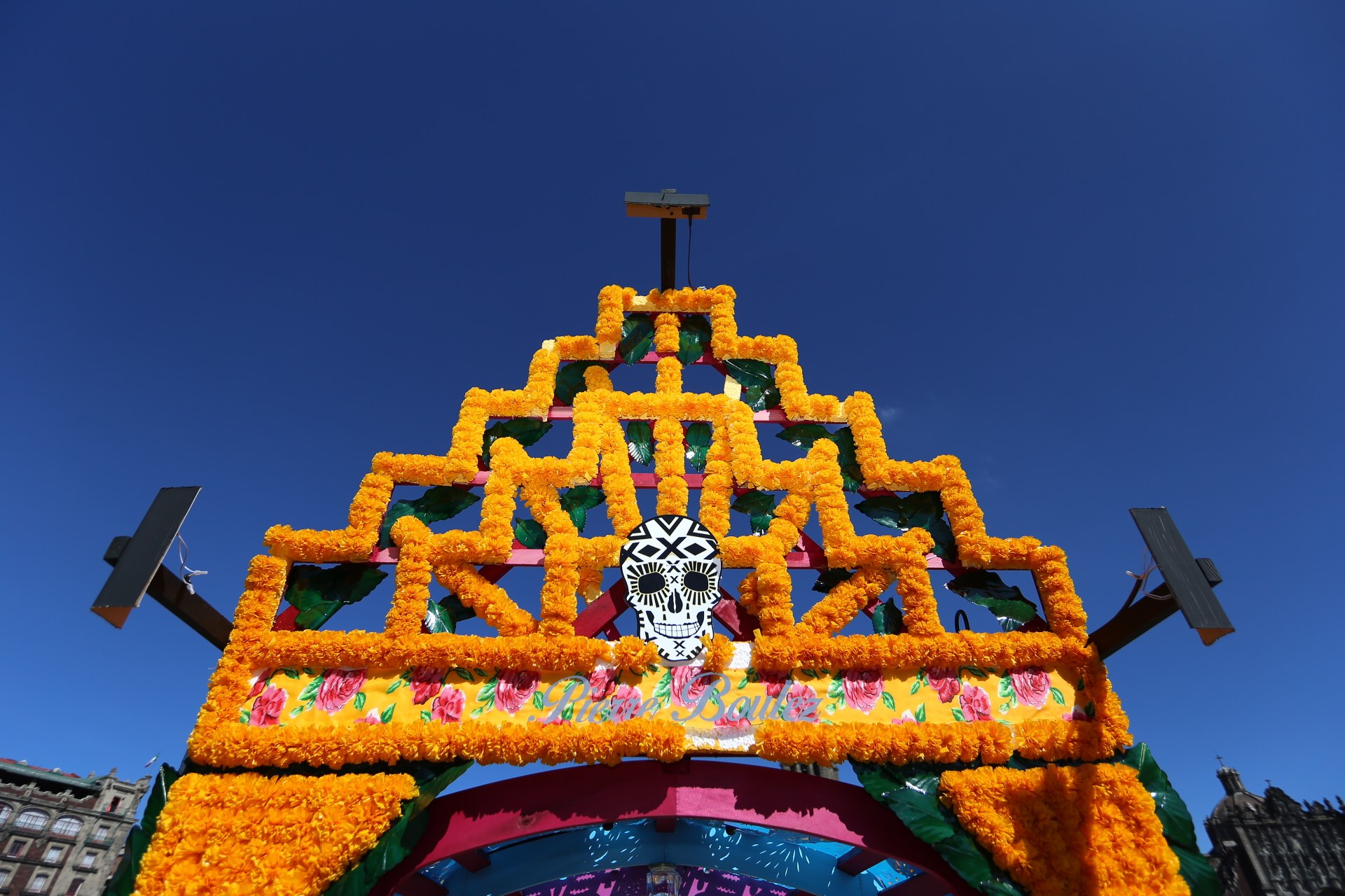 Ein Día de los Muertos-Bogen, geschmückt mit Blumen und einem Schädel, vor einem klaren blauen Himmel in Mexiko-Stadt.