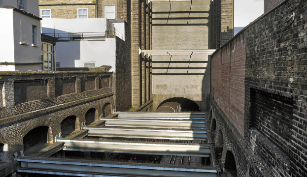 Ein Zug verlässt einen Tunnel mit Gebäuden im Hintergrund.