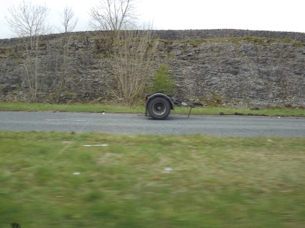 Ein Lkw-Räder auf einer Straße mit Gras, Bäumen und Felsen auf beiden Seiten.