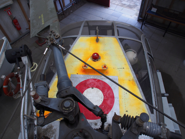 Nahaufnahme eines Hubschraubers auf einem Gebäudeboden bei der Wartung, mit einem Feuerlöscher links daneben und einer Bank rechts daneben.