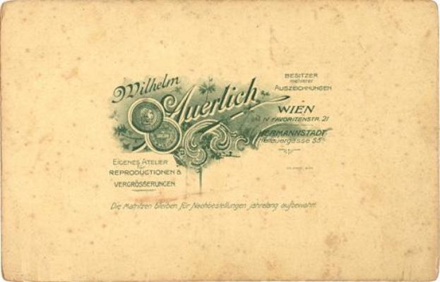 Ein altes deutsches Geldstück mit dem Porträt eines Mannes in Anzug und Krawatte mit ernster Miene, auf dem der Text "Wilhelm Auerlich Wien" gedruckt ist.