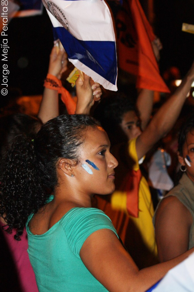 Frauen in grünen T-Shirts mit weißem Stoff, die auf einer Demonstration mit anderen Mädchen im Hintergrund stehen.