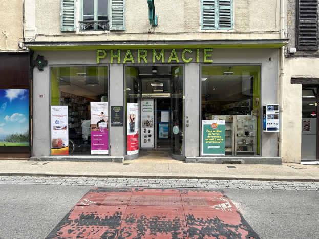 Eine Apotheke mit Glaswänden und -türen, Poster an den Wänden, an einer Straßenecke mit einer Straße unten.