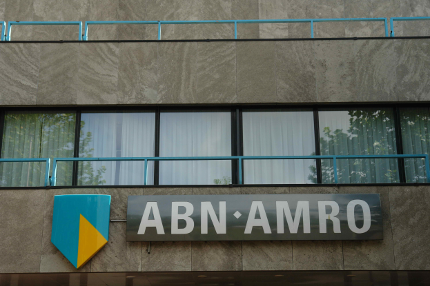 Ein Gebäude mit einer Tafel, auf der "ABN AMRO" steht, mit einer Tafel mit Text, Geländern und Glasfenstern mit Vorhängen, sowie einem Hinweis auf eine Strafe von 1,5 Milliarden US-Dollar durch die Europäische Union.