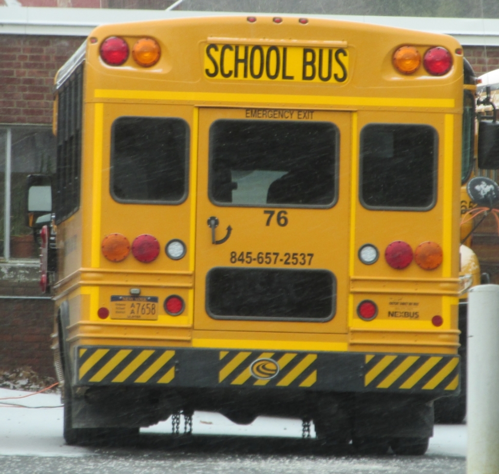Ein gelber Schulbus parkt vor einem Backsteingebäude mit Fenstern.