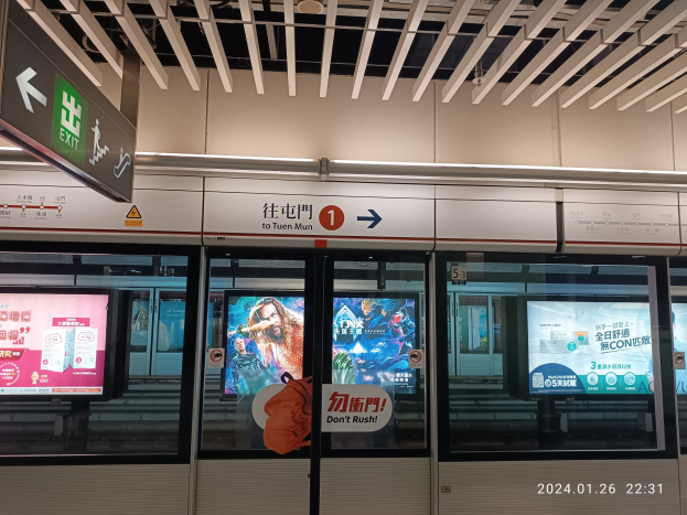Eine U-Bahn mit Glastüren und digitalen Bildschirmen an einem Bahnhof, mit beleuchteten Tafeln an der Wand und Deckenbeleuchtung.