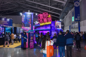 Eine große Gruppe von Menschen vor einem Stand auf einer Messe, einige halten Taschen und Schilder mit der Aufschrift 'Indie Game Development Award 2019' im Hintergrund.