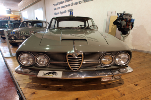 Ein klassisches Alfa Romeo Giulietta Sprint GT Junior-Modell aus den 1970er Jahren wird in einem Museum mit Seilabsperrungen und Wandtexten ausgestellt.