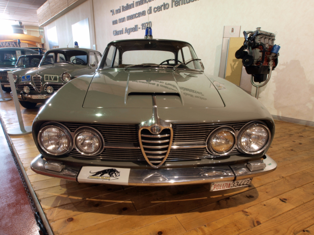 Ein klassisches Alfa Romeo Giulietta Sprint GT Junior-Modell aus den 1970er Jahren wird in einem Museum mit Seilabsperrungen und Wandtexten ausgestellt.