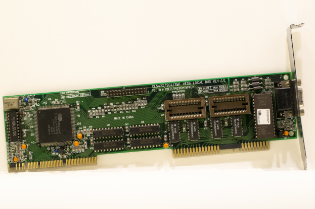 Nahaufnahme einer PCI-E-Karte mit einem zentralen Chip und mehreren angebrachten Verbindern auf einer weißen Oberfläche.