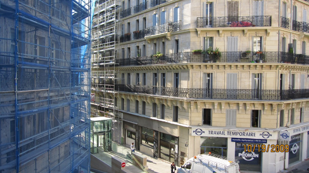 Ein großes Gebäude unter Bau auf der linken Seite, mit einem Geschäft auf der rechten Seite unten sichtbar.