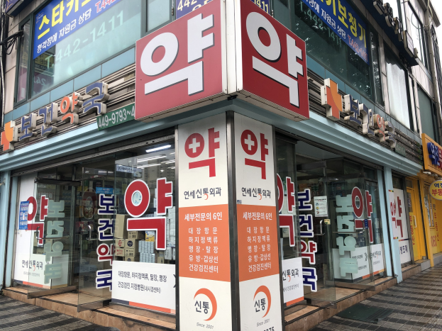 Außenansicht eines modernen Glaswand-Pharmaggebäudes in Seoul, Südkorea, mit einer Tafel, die es als Südkoreas erste Apotheke identifiziert.