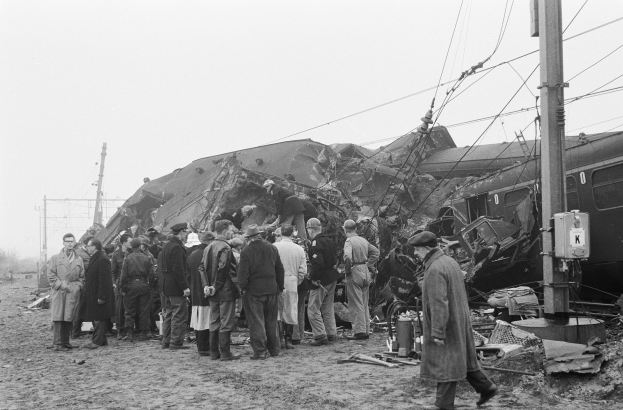 Schwarz-weißes Bild einer Gruppe von Menschen in Mützen, die in der Nähe eines Zuges stehen, der gegen einen Pfahl gekracht ist, mit Strommasten, Drähten, Bäumen und einem klaren Himmel im Hintergrund.