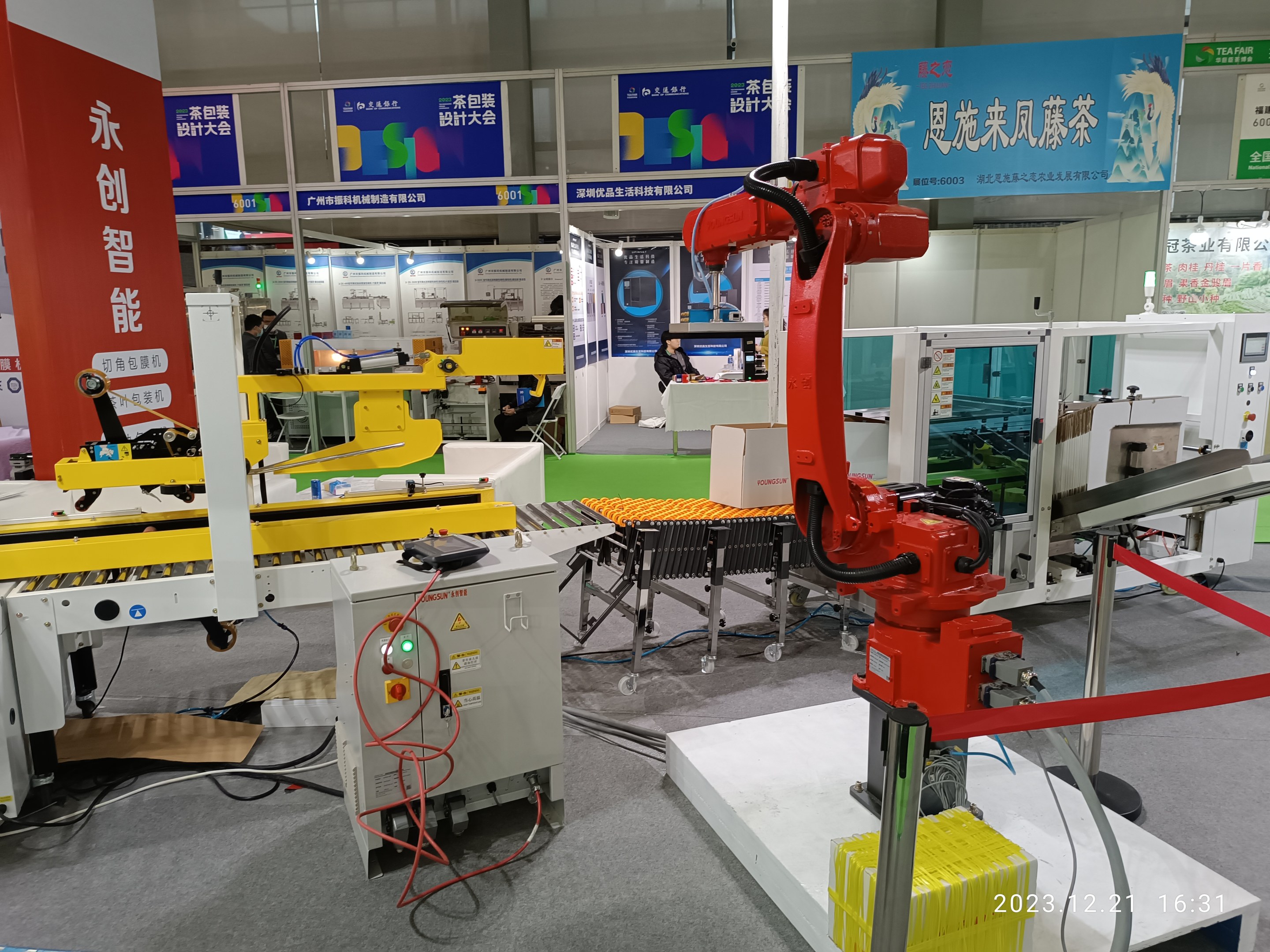 Gruppe von Robotern auf einem Tisch in einer Fabrikumgebung umgeben von Maschinen, Kabeln, Texttafeln und Beleuchtung, mit Menschen im Hintergrund.