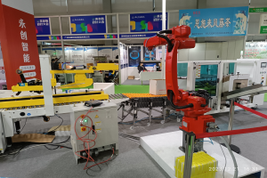 Gruppe von Robotern auf einem Tisch in einer Fabrikumgebung umgeben von Maschinen, Kabeln, Texttafeln und Beleuchtung, mit Menschen im Hintergrund.