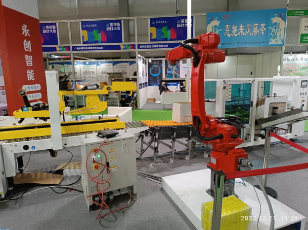 Gruppe von Robotern auf einem Tisch in einer Fabrikumgebung umgeben von Maschinen, Kabeln, Texttafeln und Beleuchtung, mit Menschen im Hintergrund.