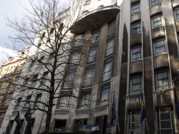 Gebäude mit Fenstern, eine Fahne und Flaggen an Stangen unten und ein Baum mit Zweigen.