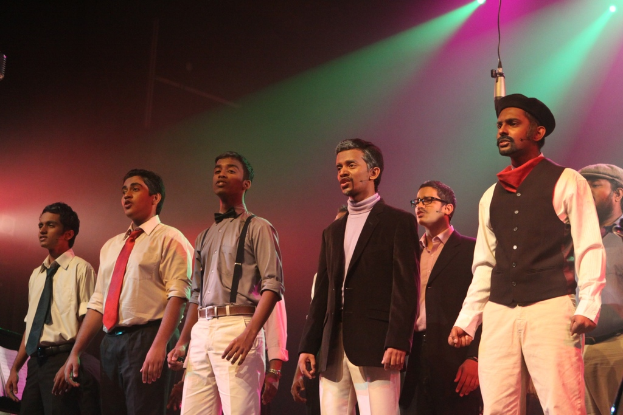 Eine Gruppe von Männern steht auf einer Bühne und spielt ein Drama mit grünen Scheinwerfern im Hintergrund.