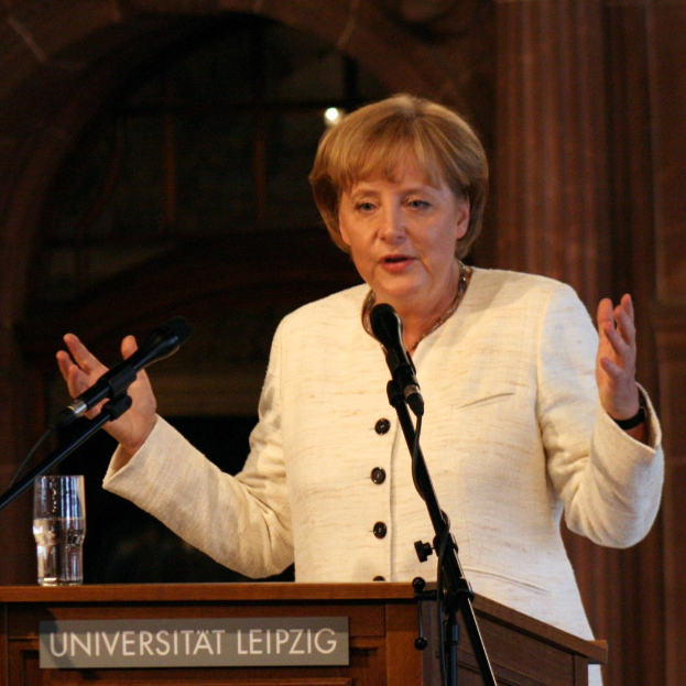 Bundeskanzlerin Angela Merkel hört eine Rede an der Universität Leipzig, hinter einem Rednerpult mit einem Mikrofon und einem Glas Wasser.