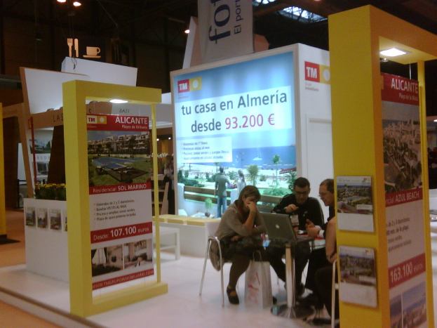 Eine Gruppe von Menschen, die an einem Tisch sitzen und auf einen Laptop schauen, mit mehreren Flyern mit verschiedenen Anzeigen daneben.