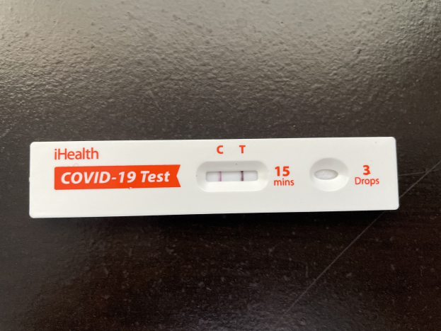 Eine schwarze Oberfl├Ąche mit einem wei├čen und roten Covid-19-Testthermometer, das Text und Zahlen anzeigt.