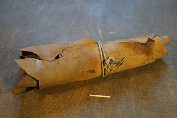 Ein brauner Papiertüte, die einer Granate ähnelt, mit einem Griff, verschnürt mit einem Seil und eine Zigarette daneben auf einem Tisch.