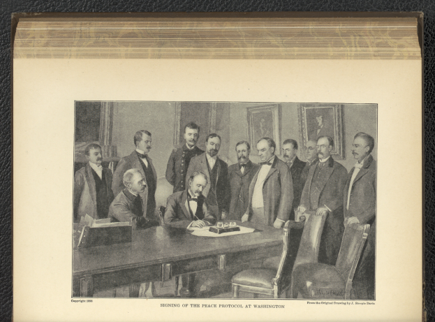 Eine Gruppe von Männern sitzt um einen Tisch mit Papieren und Gegenständen, ein Mann sitzt zentral, mit Fotorahmen an der Wand im Hintergrund und Text unten lesbar "Unterzeichnung des Friedensprotokolls in Washington".