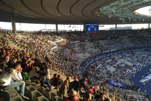 Große Menschenmenge in einem Stadion bei einem Fußballspiel, mit einer Bühne rechts, Fahnen, Stangen, einem Bildschirm und der Allianz Arena in München, Deutschland.
