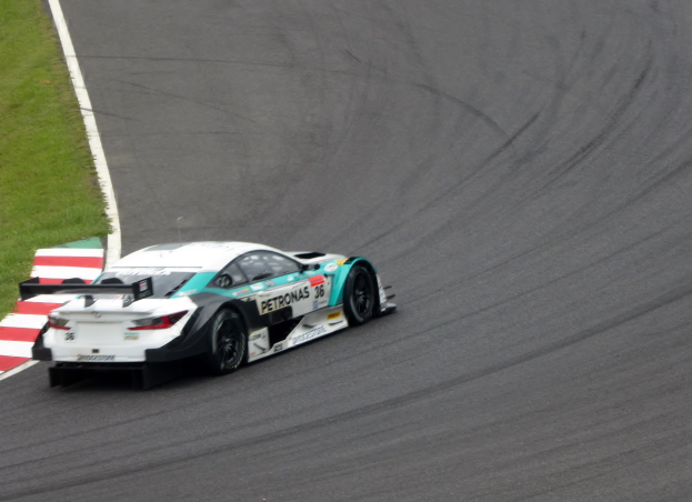 Ein silberner Mercedes-AMG GT3-Rennwagen mit Sponsorentext auf der Karosserie, der auf einer Rennstrecke fährt, mit Gras auf der linken Seite.