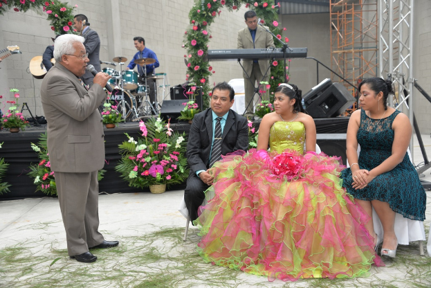 Ein Mann steht vor einem Mikrofon, während andere sitzen und ein Orchester im Hintergrund spielt.