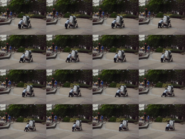 Ein Kind geht auf einer Straße und zieht einen Karren, mit zwei Personen, die Fahrräder halten, auf der linken Seite und einem Gebäude und Bäumen im Hintergrund.