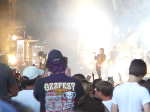 Eine Gruppe von Menschen in verschiedenen Kleidungsstücken, einige mit Mützen, in der Nähe von Musikinstrumenten wie einer Gitarre und einem Mikrofon mit Bühnenbeleuchtung.