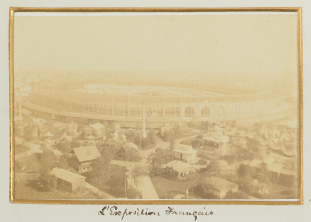 Altes Schwarz-Weiß-Foto eines Stadions, umgeben von Stadtgebäuden, Bäumen und Strommasten mit Text am unteren Rand.