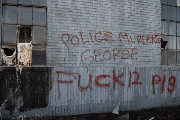 Ein Gebäude mit der Graffiti-Beschriftung "Polizei M"rdet George Fuck 12 P19" an seiner Seite, das Fenster und verschiedene Gegenstände vor ihm zeigt.