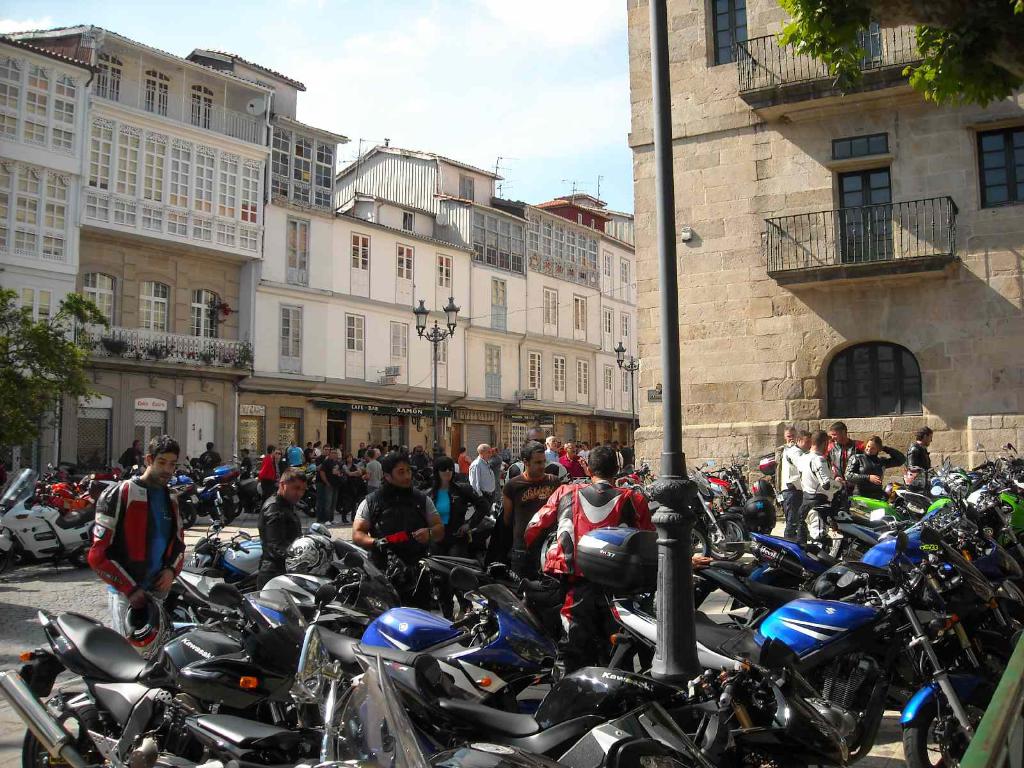Ein cremefarbenes Gebäude mit zahlreichen Fenstern, das an ein Backsteingebäude mit einer Metallbalustrade angrenzt, mit mehreren Fahrrädern, die davor geparkt sind, und Menschen, die sich unterhalten.
