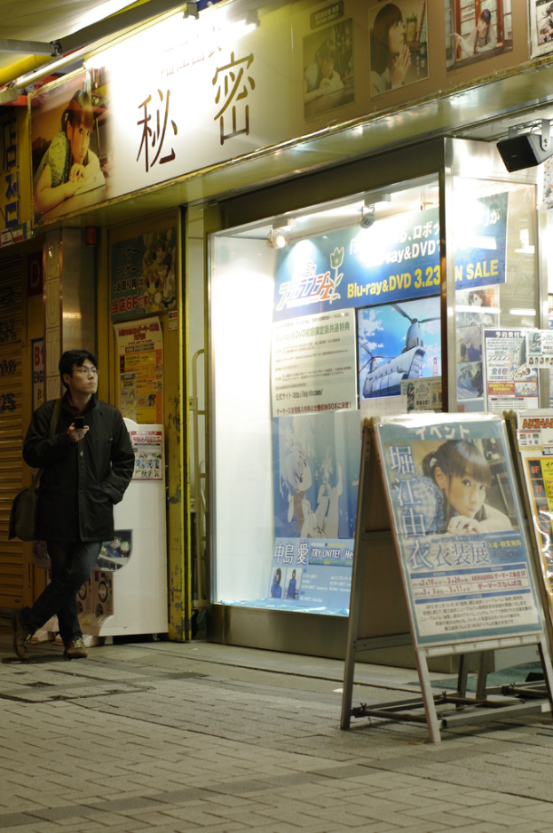 Ein Mann steht mit einem Mobiltelefon in der Hand, trägt eine Tasche und hält Schilder mit Text, Geschäfte, Lichter und Papiere mit Text im Hintergrund.