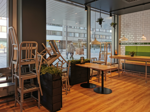 Ein Berliner Restaurant mit Holztischen und -stühlen vor einem großen Fenster, das eine Straßenszene mit Fußgängern, Gebäuden und Grün zeigt.