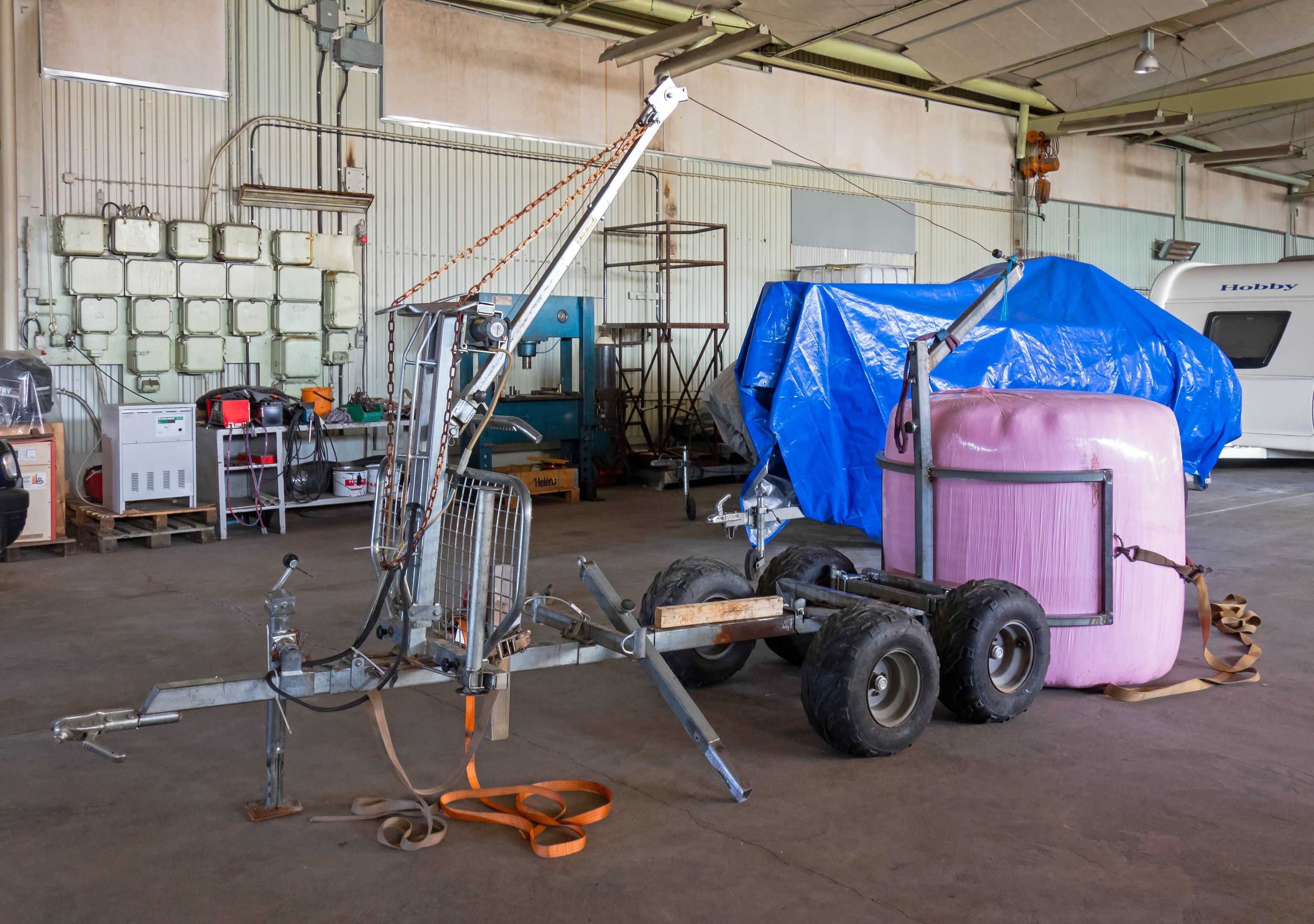 Blauer Planen-Auflieger an einem Fahrzeug in einer Garage mit Gegenständen auf dem Boden und beleuchteten Wänden im Hintergrund.