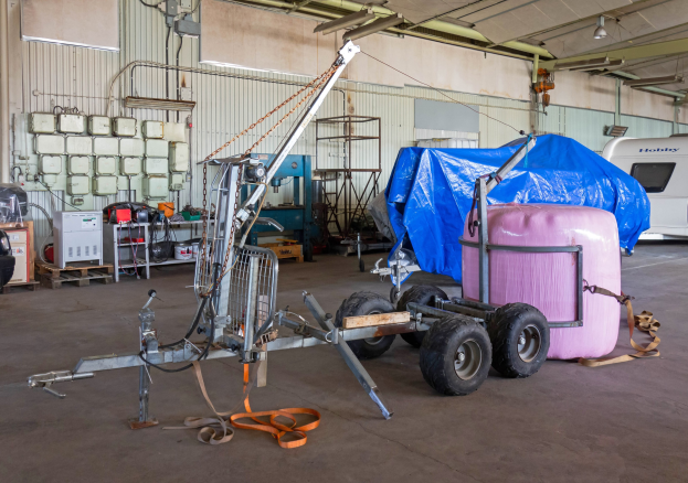 Blauer Planen-Auflieger an einem Fahrzeug in einer Garage mit Gegenständen auf dem Boden und beleuchteten Wänden im Hintergrund.