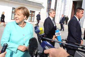 Bundeskanzlerin Angela Merkel spricht vor der Kanzleramt in Berlin mit Reportern, umgeben von Menschen, einige halten Mikrofone, mit Gebäuden im Hintergrund.